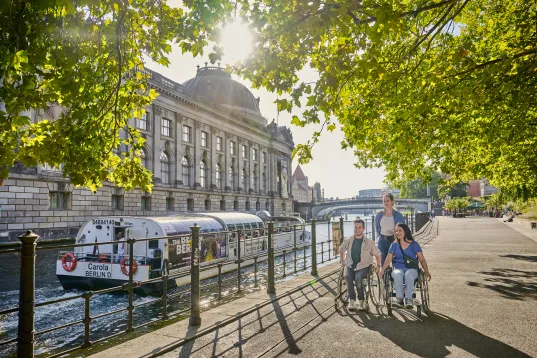 Two wheelchair users with accompanying persons on the shore of Museum Island