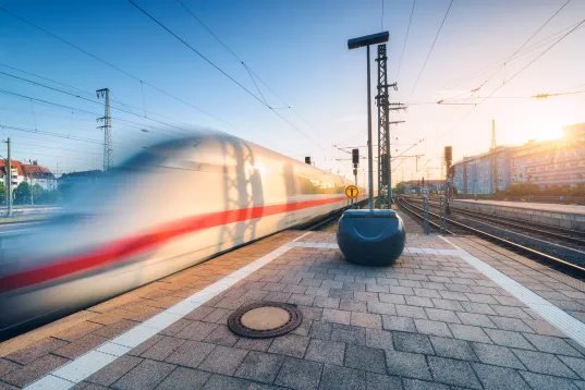 White high speed train in motion on the railway station at sunset. Germany. Blurred modern intercity train on the railway pl…