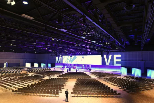 Large, empty conference hall with rows of chairs and a brightly lit stage.