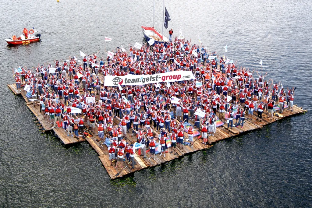 A large crowd on a raft, holding banners, floating on the sea.