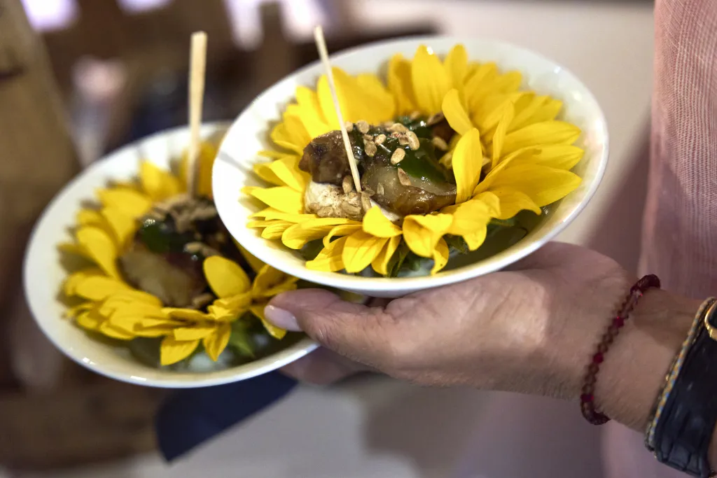 Zwei Teller mit gelber Sonnenblume und kleinen Häppchen, von einer Hand gehalten.