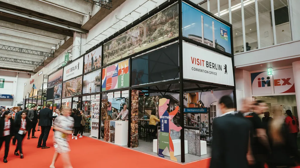 Visitors walk through the exhibition hall past the colorful visitBerlin booth featuring images of the city.